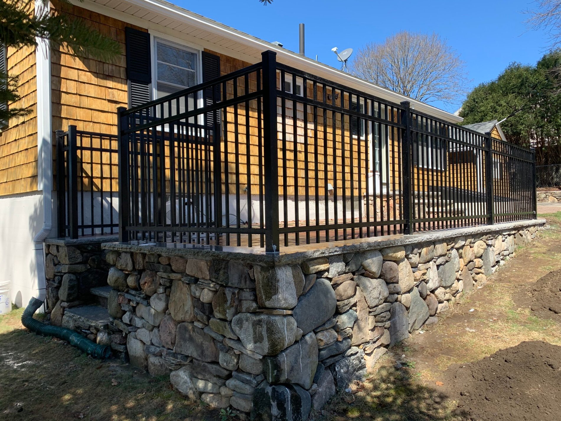 Black ornamental aluminum fence set on a fieldstone wall by Prime Fence